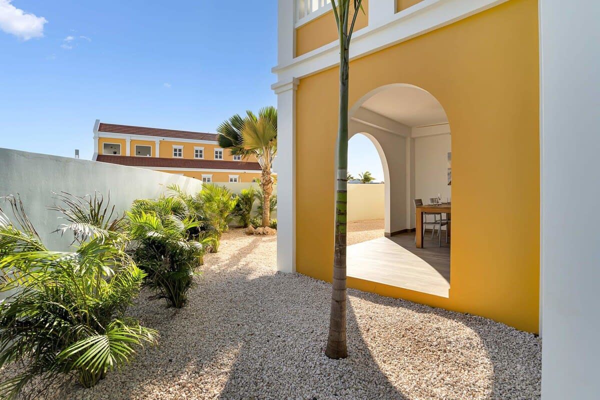 A courtyard with a palm tree, gravel path, and a building with yellow walls and a white archway.