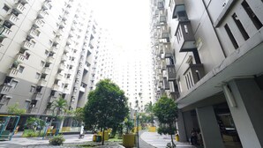 Een hoog appartementencomplex met balkons, een groen middenterrein met bomen, en een voetpad.