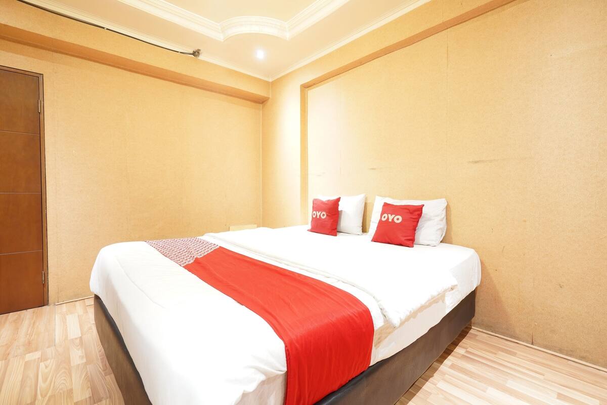 Une chambre d’hôtel avec un grand lit, une armoire en bois et un mur uni.