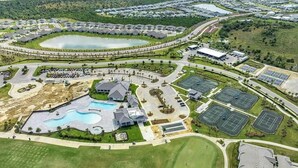 Vue aérienne d’un quartier résidentiel avec une grande piscine, des courts de tennis et un terrain de golf.