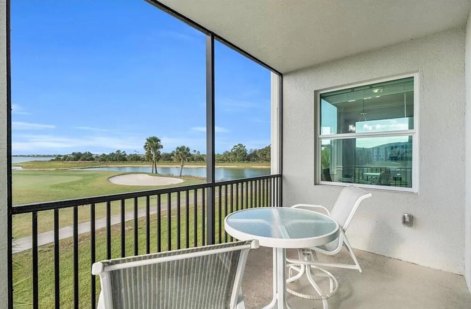 A balcony with a glass table and chairs, overlooking a golf course and a body of water.