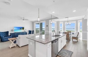 A modern kitchen with a central island, white cabinetry, and a view of the ocean through large windows. - Golf included! Fabulous golf, lake, & sunset views. Walk to the resort pools. (Punta Gorda)