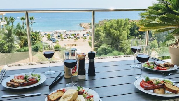 A table with plates of food and wine glasses, overlooking a beach and ocean view.