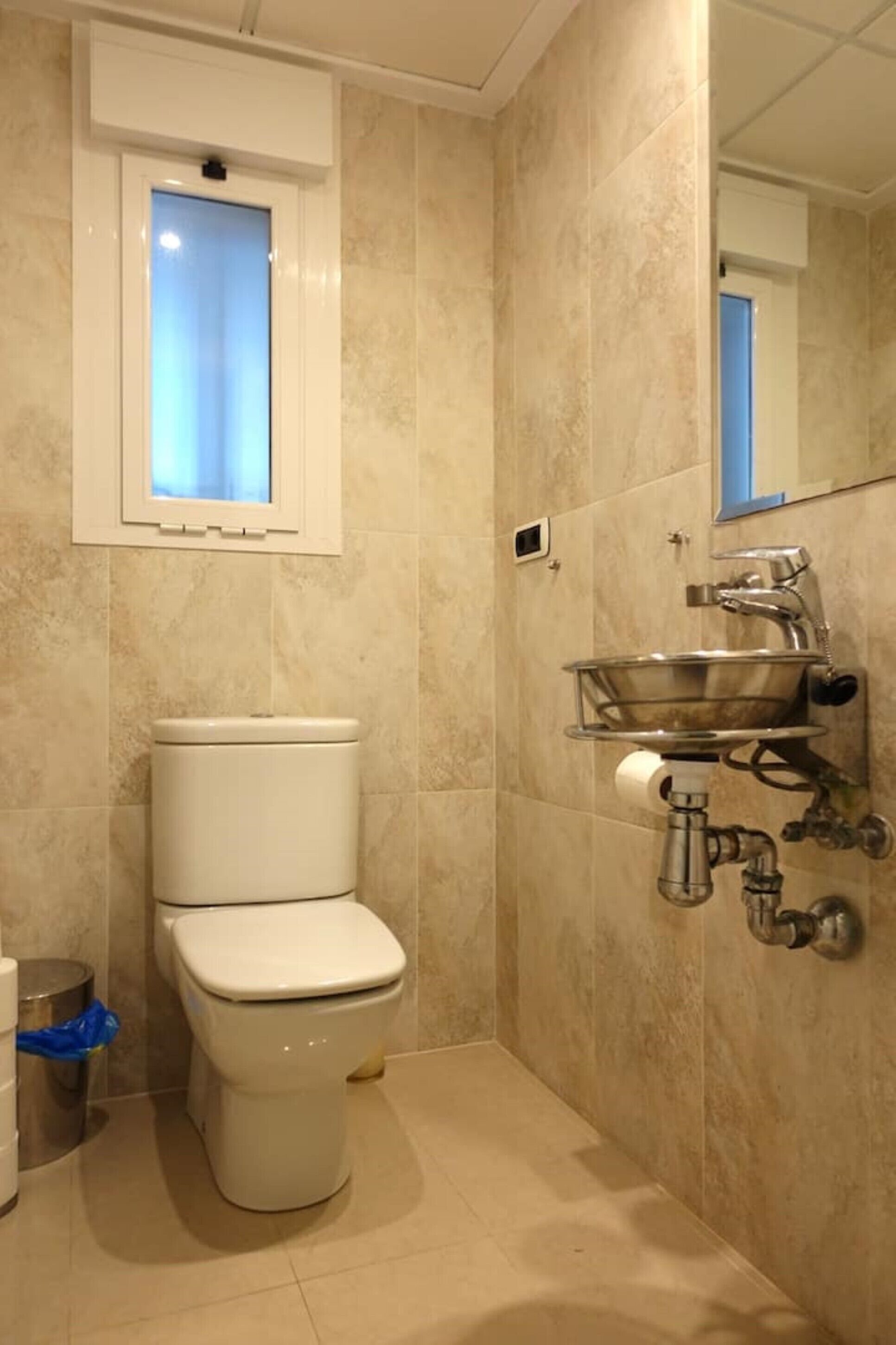 A bathroom with a toilet, a wall-mounted sink, and a mirror.