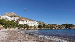 A coastal area with a building complex, a rocky beach, and a clear sky.