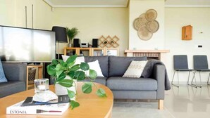 A modern living room with a grey sofa, a coffee table with a book and a plant, a TV, and a bookshelf with decorative items.