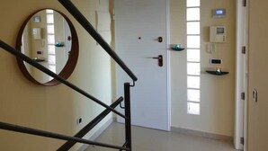 A hallway with a white door, a round mirror, and a thermostat on the wall.
