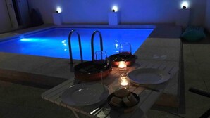 A poolside dining setup with a table, plates, a candle, and a bowl of fruit.