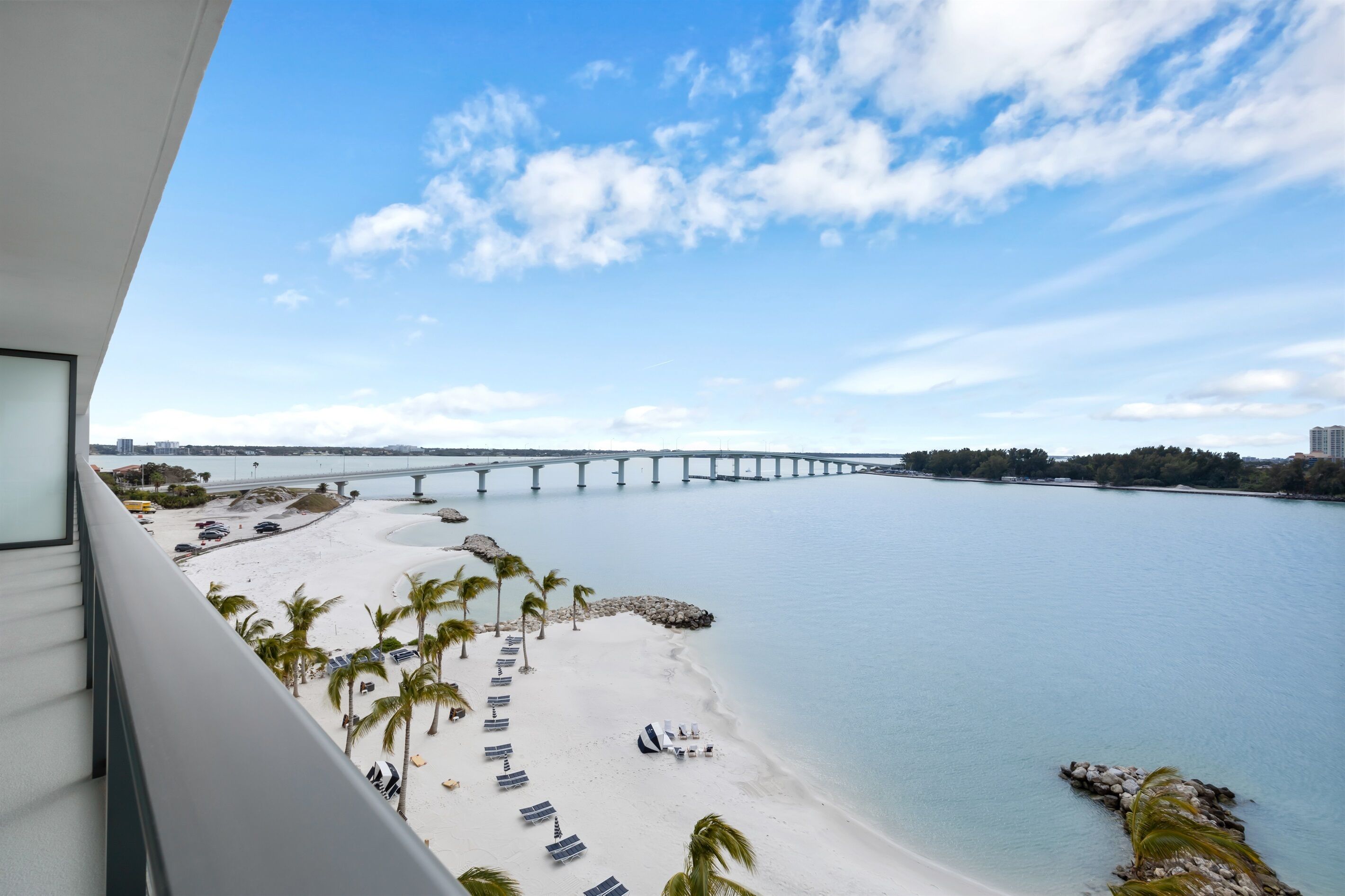 A beach with a bridge in the background, palm trees, and a clear sky.