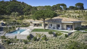 A modern house with a swimming pool, outdoor seating, and a view of the surrounding landscape.