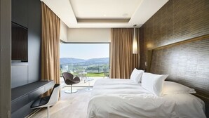 A modern hotel room with a large bed, a flat-screen TV, a seating area with chairs, and a view of the outdoors.