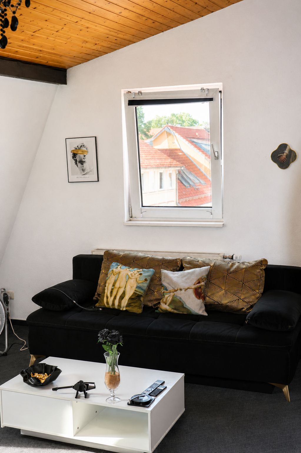 Ein Wohnzimmer mit einer schwarzen Couch, einem weißen Couchtisch, einem gerahmten Bild und einem Fenster mit Blick auf ein Gebäude.