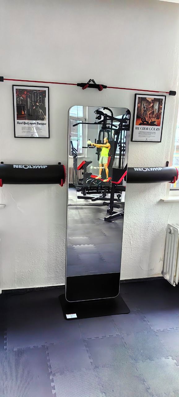 Ein Fitnessraum mit NEOLAMP-Geräten, einer Spiegelwand und gerahmten Bildern.