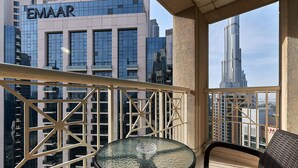 A balcony with a glass table and chairs, overlooking a cityscape with modern buildings and a prominent skyscraper.