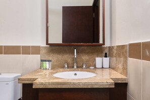 Bathroom features a central sink, large mirror, and small cabinet with toiletries.