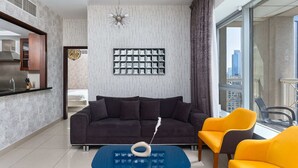 A modern living room with a dark sofa, a blue coffee table, and a yellow armchair. A decorative wall piece is above the sofa.