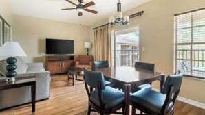 A hotel room with a dining table, chairs, a sofa, a TV, and a ceiling fan. - Aqua Sol is a fun family adventure! (Winter Garden)