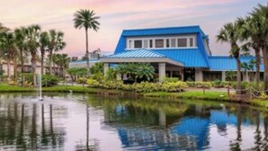 A building with a blue roof and a reflection in the water. - Aqua Sol is a fun family adventure! (Winter Garden)