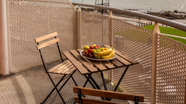 A balcony with a table and two chairs, overlooking a body of water.