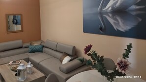 A modern living room with a sectional sofa, a coffee table with decorative items, a wall-mounted mirror, and a large painting of a swan. - Swan Paradise Glyfada Apartment  (Glyfada)