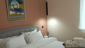 A neatly made bed with white linens and pillows, a bedside table with a vase of flowers, and a wall-mounted air conditioner. - Swan Paradise Glyfada Apartment  (Glyfada)