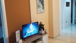A living room with a television on a white cabinet, a small Christmas tree, and a painting on the wall. - Swan Paradise Glyfada Apartment  (Glyfada)
