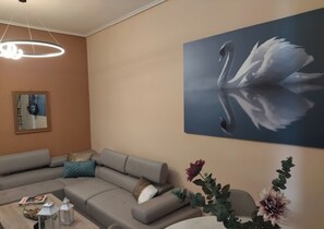Una sala moderna con un sofá seccional, una mesa de centro con objetos decorativos, un espejo montado en la pared y un cuadro grande de un cisne.