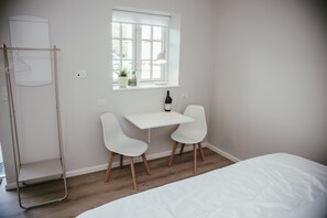 A bedroom with a bed, a desk, two chairs, a window, and a hanging light fixture.