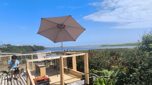 Une terrasse en bois avec une table et des chaises, un parasol et une vue sur la mer.