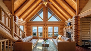 A log cabin interior with a high ceiling, wooden walls, a fireplace, and a seating area with sofas and a coffee table. - 4 Kings Log Cabin 150 Acres Spectacular Views (Three Rivers)