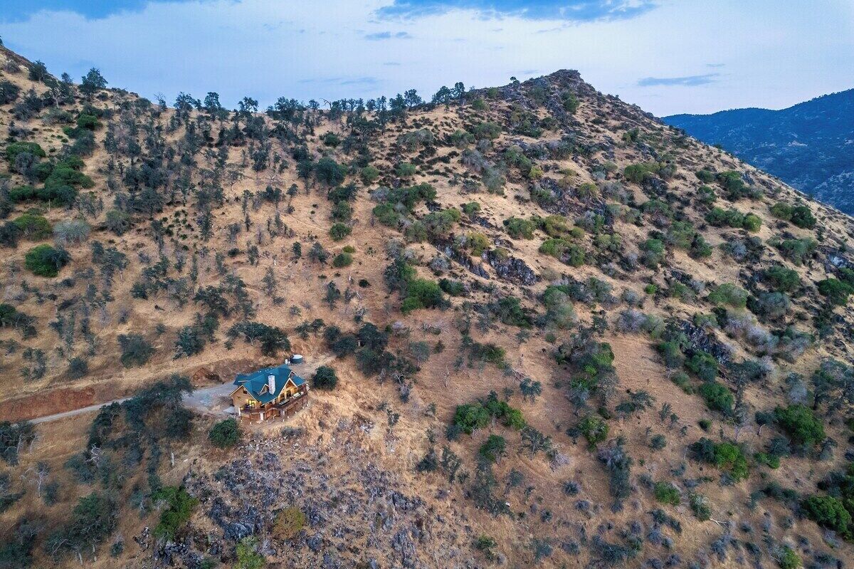 Una casa aislada de un solo piso con techo inclinado, rodeada de terreno árido y montañoso con vegetación escasa.