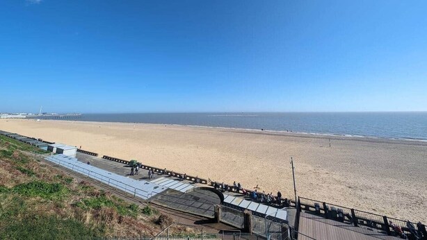 A beach with a long pier extending into the sea, a clear sky, and a few people walking along the shore. - Myana Nest (Lowestoft)