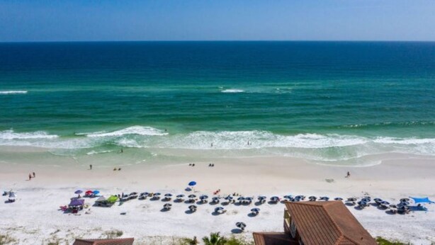Uma praia com areal dourado, guarda-sóis e um edifício com telhado vermelho.
