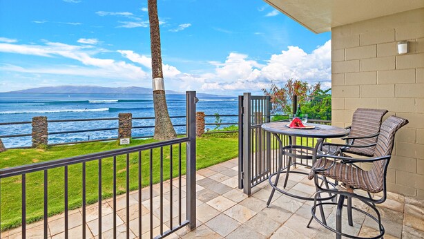 A balcony with a view of the ocean, a table with chairs, and a potted plant. - Oceanfront Studio w/Sunsets and Surf - Noelani 119 - Turtle Viewing Beach (Lahaina)