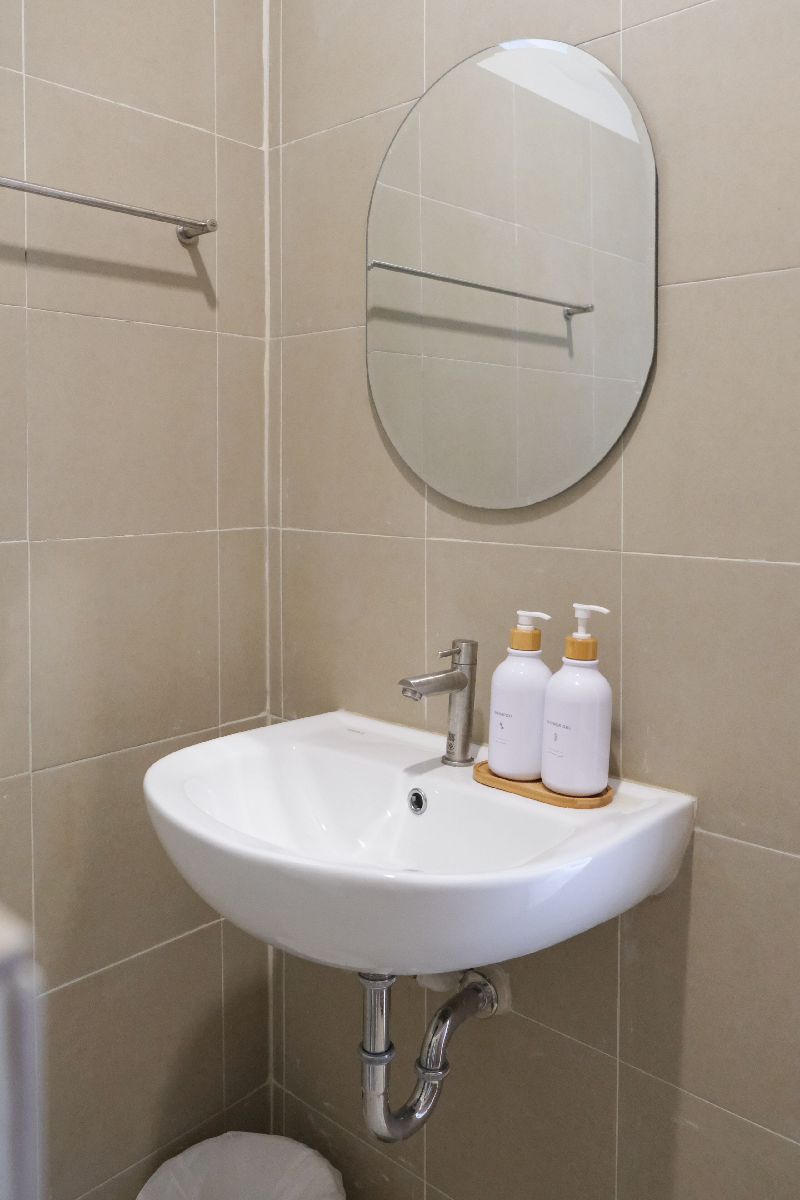 Un baño con un lavamanos blanco, un espejo redondo y dos botellas de champú sobre el lavamanos.