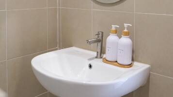 Un baño con un lavamanos blanco, un espejo redondo y dos botellas de champú sobre el lavamanos.