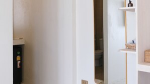 A hallway with a white door, a mirror, and a small shelf with toiletries. - Nymph Hideout (Ko Pha-ngan)