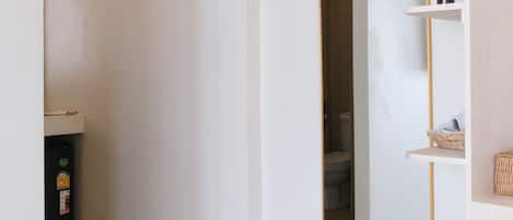 A hallway with a white door, a mirror, and a small shelf with toiletries.