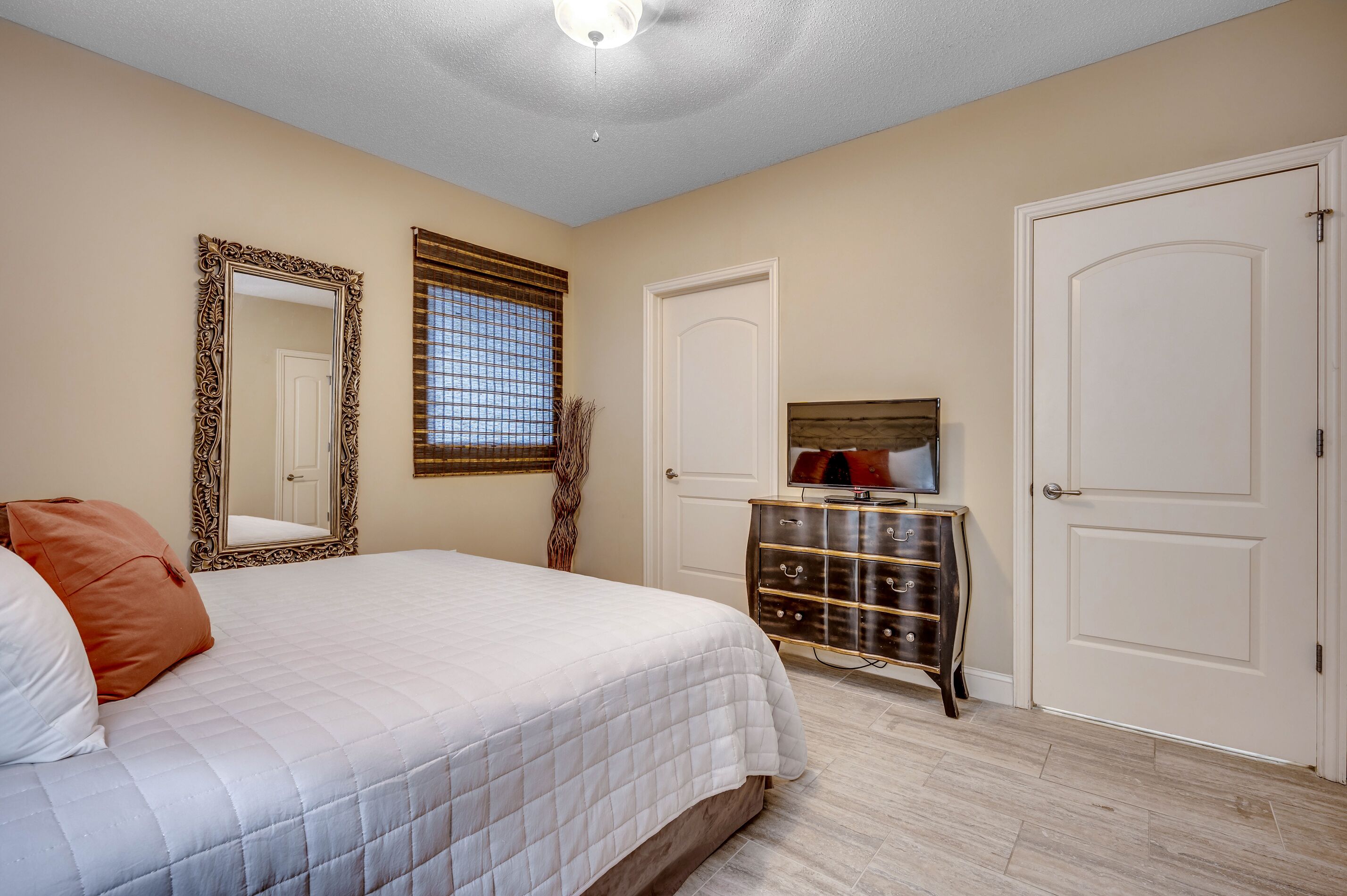 A bedroom with a bed, a dresser, a television, and two doors.