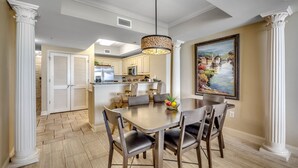 A dining area with a wooden table and chairs, a hanging light fixture, and a painting on the wall.
