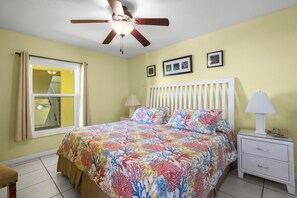 Ein Schlafzimmer mit Bett, Nachttisch, Lampe, Deckenventilator und einem Fenster mit Vorhängen.