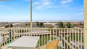 A balcony with a table and chairs, overlooking a beach and palm trees. - 🌞 South Beach Condo #503 Gulf Front Serenity with Balcony on Treasure Island (Treasure Island)