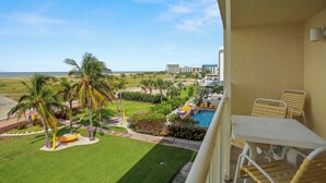 A balcony with a view of a pool, palm trees, and a beach.