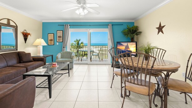 A living room with a sofa, coffee table, TV, dining table with chairs, and a ceiling fan.