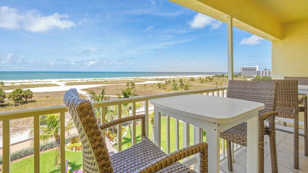 A balcony with wicker furniture, a white table, and a view of the beach and ocean.