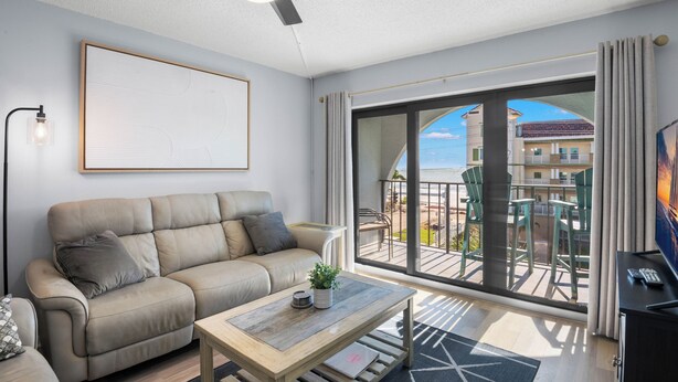 Un salon moderne comprenant un canapé, une table basse, un ventilateur de plafond et une grande fenêtre donnant sur l’extérieur.