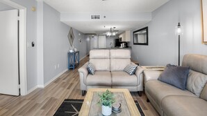 Un salon avec un canapé beige, une table basse ornée d’une plante et un ventilateur de plafond.