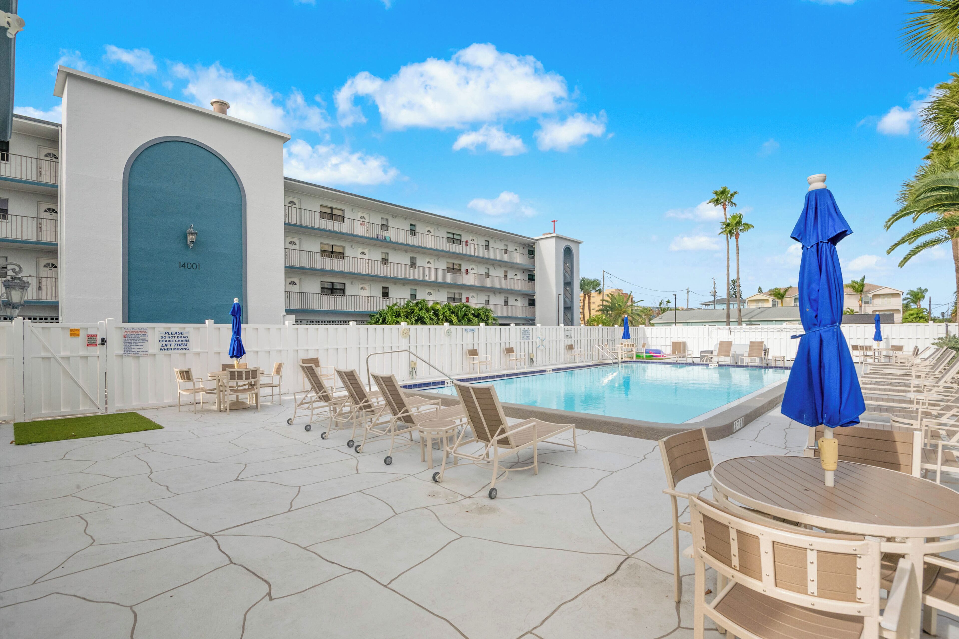 A pool area with lounge chairs and umbrellas, a building with a large arched entrance, and a clear blue sky.