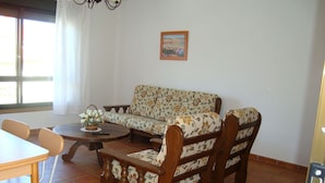 A living room with a sofa, chairs, a table, and a window with curtains. - Apartamento EN EL Rural CON Terraza EN Sanxenxo, Cerca DEL MAR (Rebel- Vilalonga, Sanxenxo)