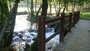 A wooden bridge over a flowing stream, surrounded by trees and a stone building. - Apartamento EN EL Rural CON Terraza EN Sanxenxo, Cerca DEL MAR (Rebel- Vilalonga, Sanxenxo)